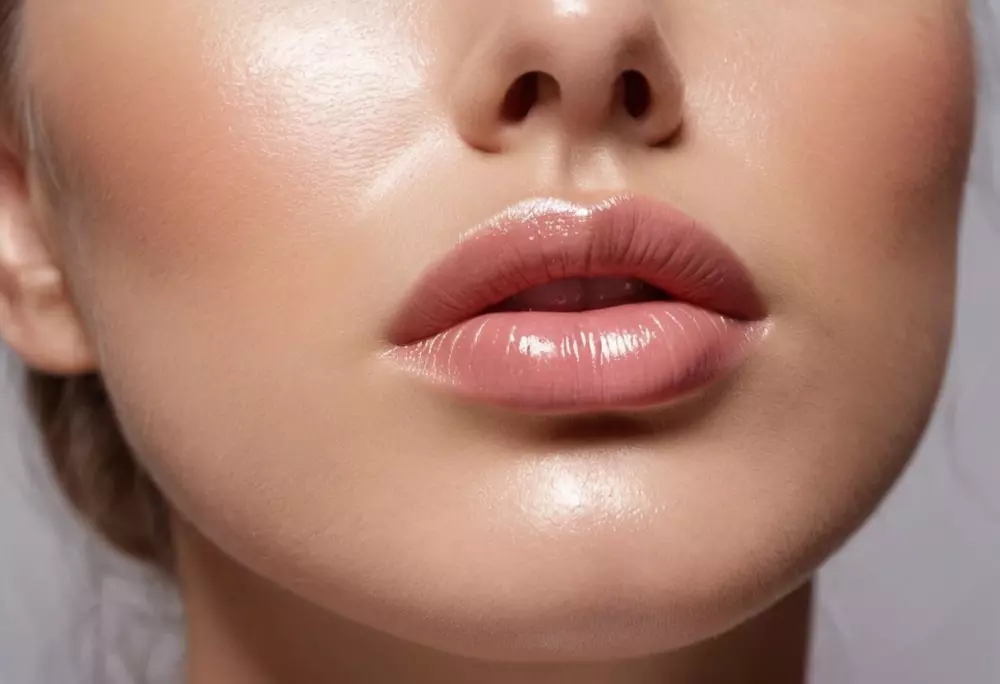 Eine Person trägt eine feuchtigkeitsspendende Gel-Lippenmaske auf, wobei der Fokus auf den Lippen und der glänzenden Textur der Maske liegt, Nahaufnahme, fotografisch festgehalten, die klare und feuchte Oberfläche der Lippenmaske wird mit weichem Studio-Licht in hoher Auflösung hervorgehoben.