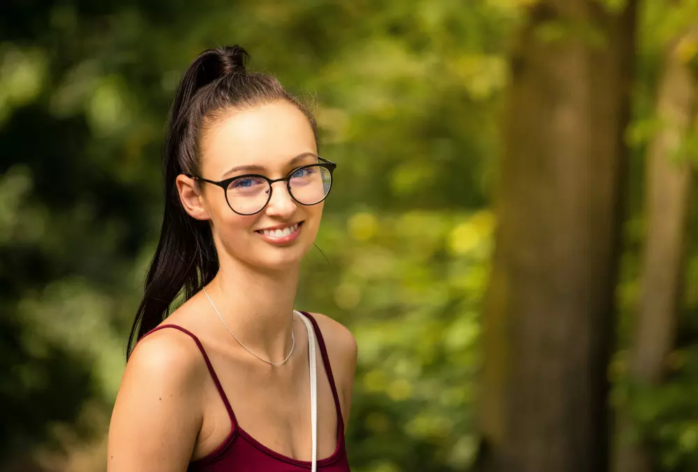 a woman wearing glasses standing in front of trees