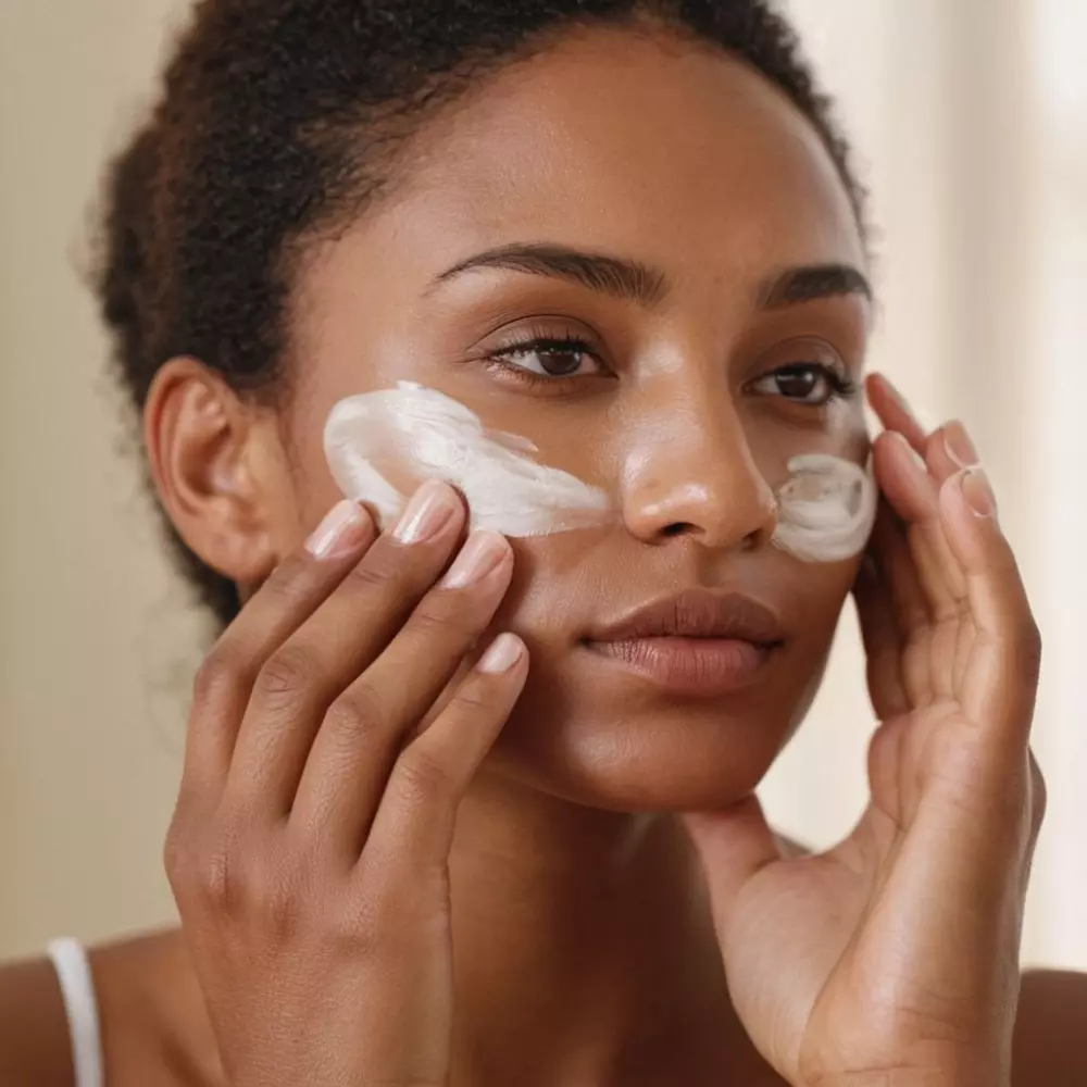 Close-up of hands applying moisturizer on the face gently, under warm, natural light, in a clean, serene setting, photographed with a 50mm lens, high resolution.