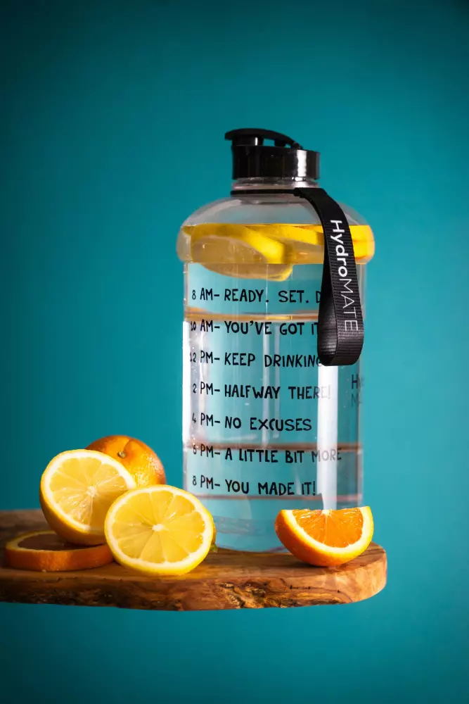 a glass water bottle with lemons on a cutting board