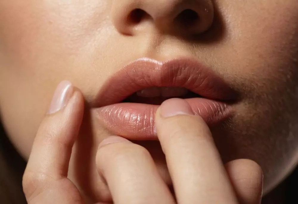 Nahaufnahme von den Lippen einer Person, die sanft von der eigenen Fingerspitze berührt werden, unter weichem, diffusen Licht, in einem detailreichen, fotografischen Stil.