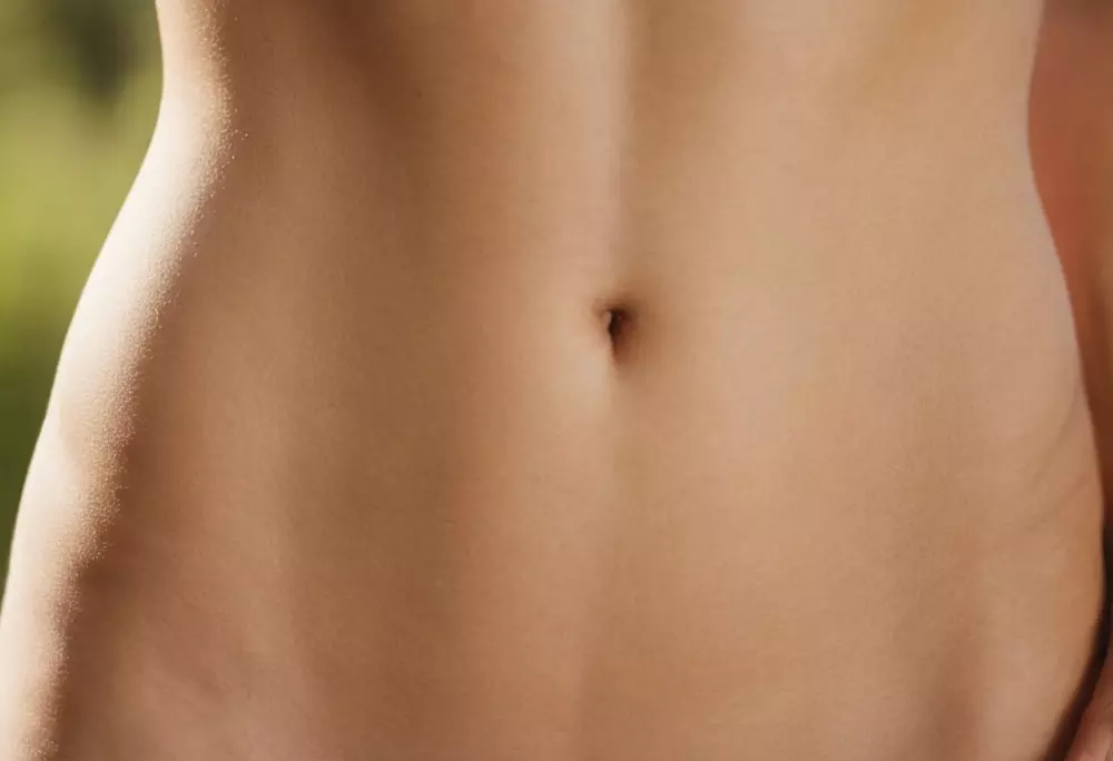 Nahaufnahme eines trainierten Bauches im weichen Fokus, im Freien, vermittelt das Konzept der Hautfestigkeit ohne chirurgischen Eingriff, Fotografie, aufgenommen mit einem mittleren Teleobjektiv bei natürlichem Licht.