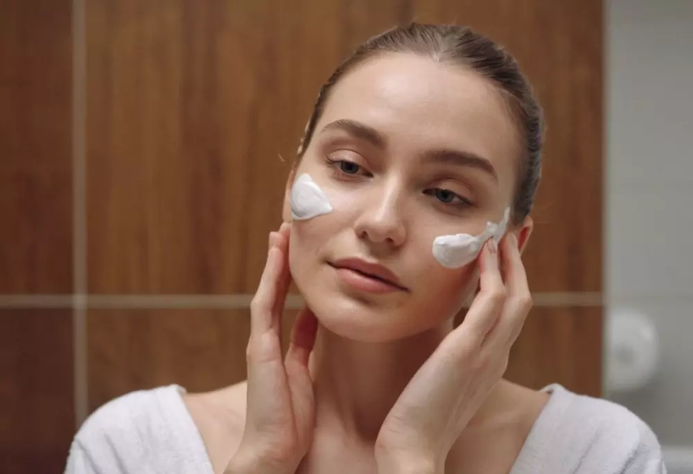 Hautpflegeroutine für Gesichtsgymnastik, eine Frau trägt sanft Feuchtigkeitscreme auf ihr Gesicht auf, steht in einem Badezimmer mit sauberem, hellem Design, Nahaufnahme, fotografischer Stil, Verwendung von natürlichem Licht, detailliert mit hoher Auflösung.