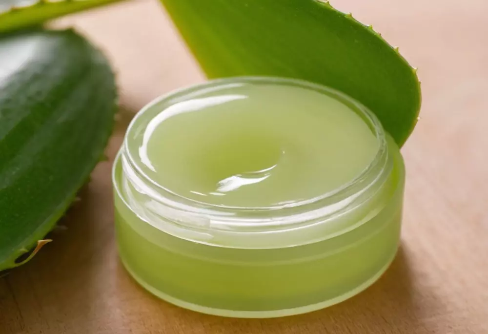 Nahaufnahme eines Aloe Vera Lippenbalsams in einem geöffneten Behälter, Fokussierung auf die grüne, gelartige Textur des Balms, in einer hellen und sauberen Umgebung, Fotografie mit einem Makroobjektiv und Weichzeichnung, um die Textur zu betonen.