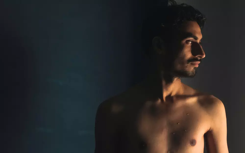 Un hombre sin camisa de pie junto a una pared