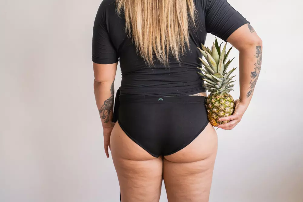 Eine Frau in einem schwarzen Badeanzug hält eine Ananas.