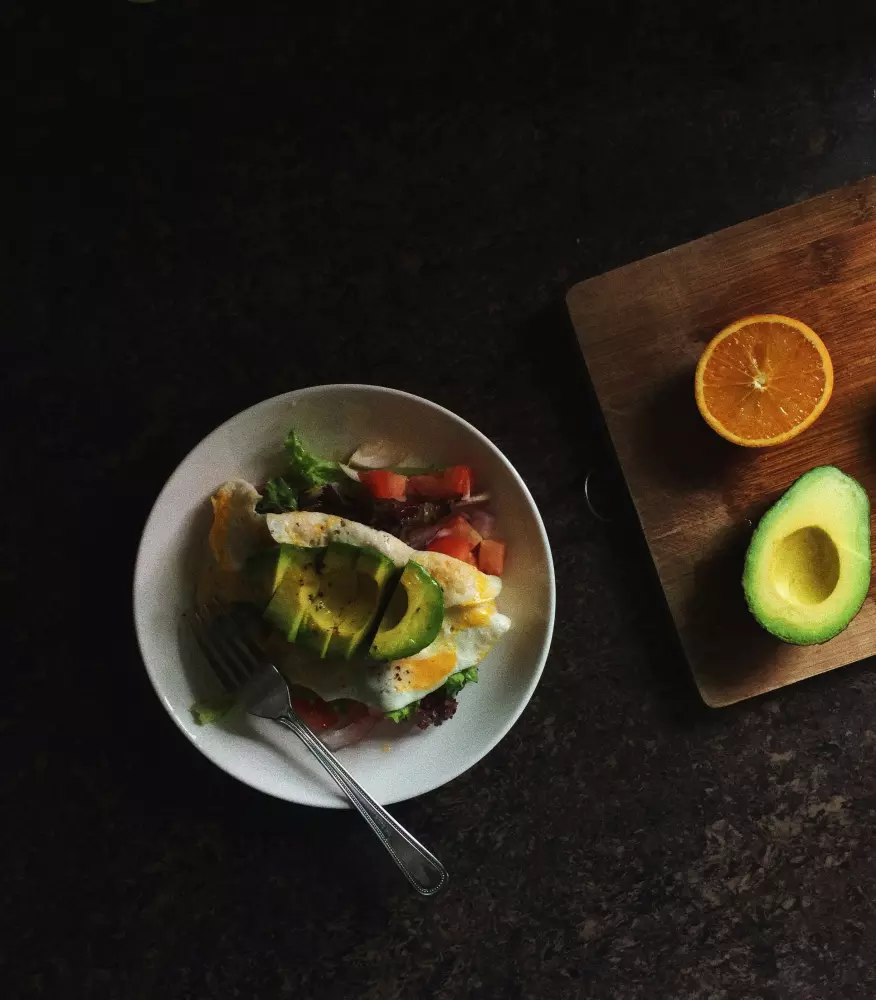Ein Teller mit Essen, einer Avocado und einer Orange auf einem Schneidebrett.