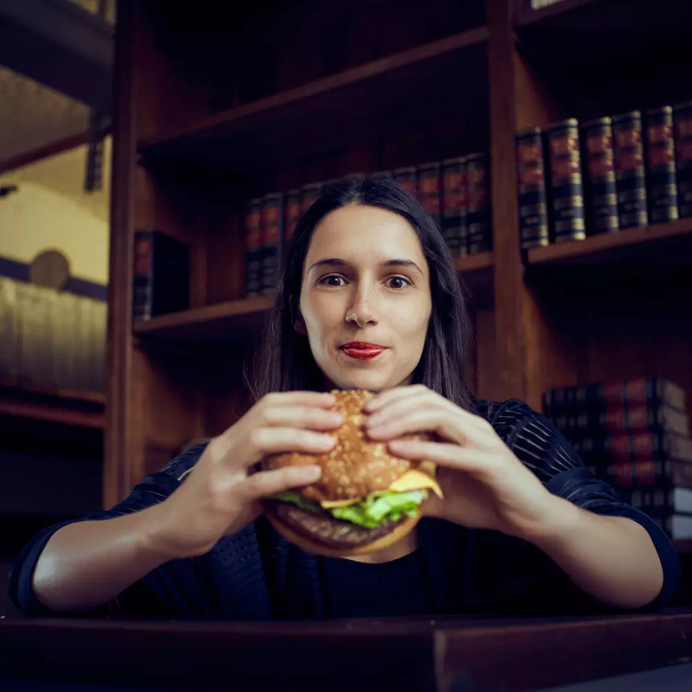 Eine Frau hält einen Hamburger vor ihr Gesicht.