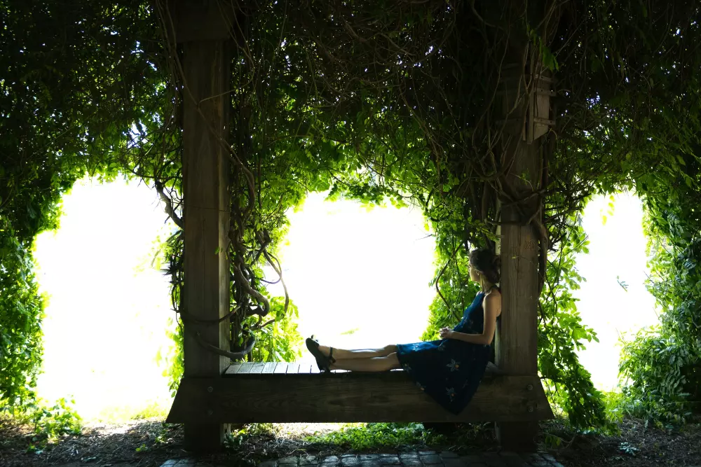 Eine Frau sitzt auf einer hölzernen Bank, die mit Ranken bedeckt ist.