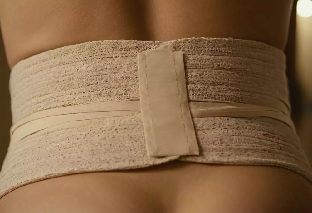 Una foto en primer plano de una cintura con vendajes postoperatorios, centrándose en los detalles del cuidado, en una sala de recuperación con una iluminación suave. Fotografía realizada con un lente macro para capturar la textura y los detalles de los vendajes y la piel, asegurando una imagen clara y detallada.