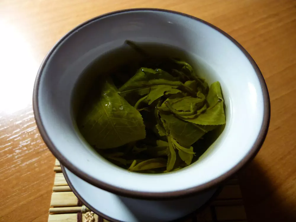 un bol blanco lleno de hojas verdes encima de una mesa de madera