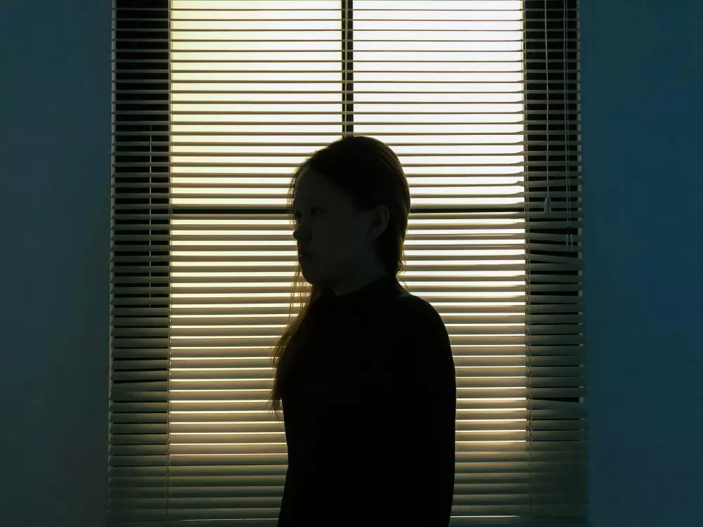 a woman standing in front of a window with blinds