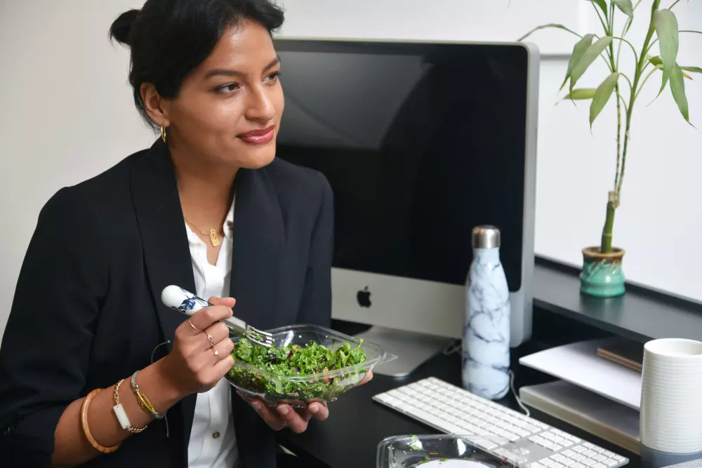 Eine Frau sitzt an einem Schreibtisch und hält eine Schale mit grünem Gemüse.