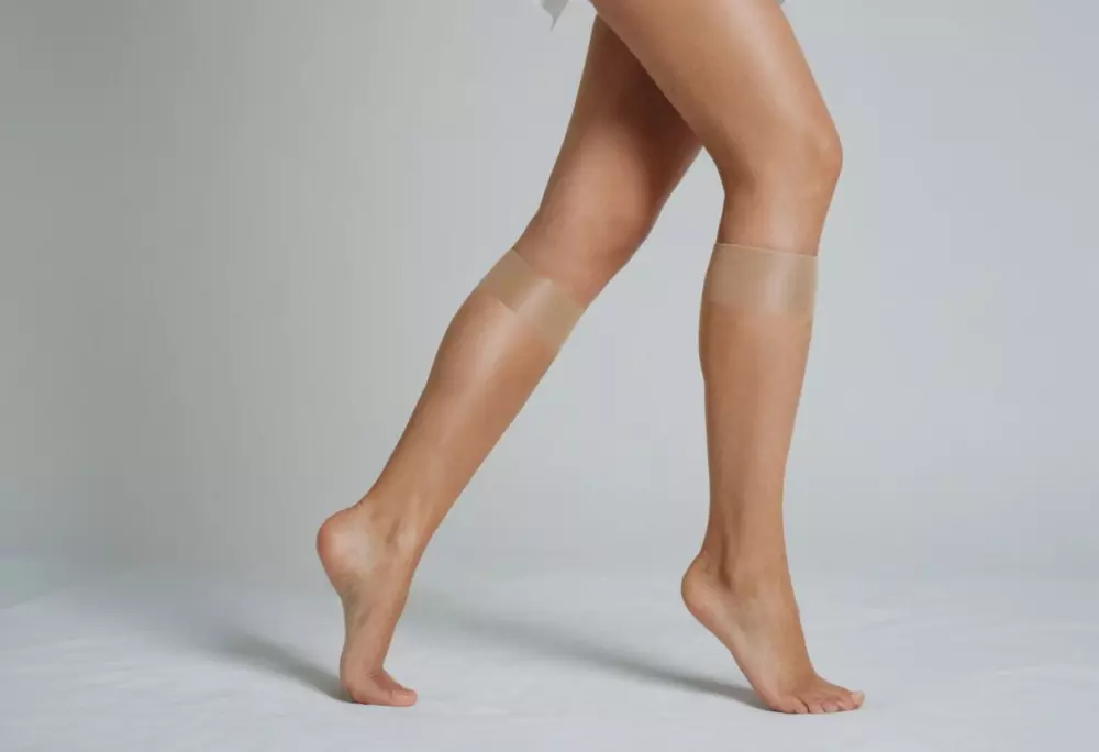 Kompressionsbekleidung, die an den unteren Gliedmaßen getragen wird, detaillierte Ansicht des Stoffes und der Passform an den Beinen, vor einem sauberen, einfachen Hintergrund. Fotografie, aufgenommen mit scharfem Fokus, um die Textur und Passform der Kleidungsstücke hervorzuheben.