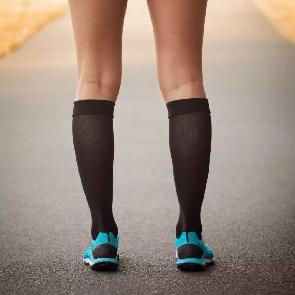 Nahaufnahme von Beinen, die Kompressionsstrümpfe tragen, mit Fokus auf dem Wadenbereich, vor einem Hintergrund mit Farbverlauf, der auf eine Druckverteilung hinweist, im fotografischen Stil, aufgenommen mit natürlichem Licht und einem 50mm Objektiv für eine detaillierte Textur-Sichtbarkeit.