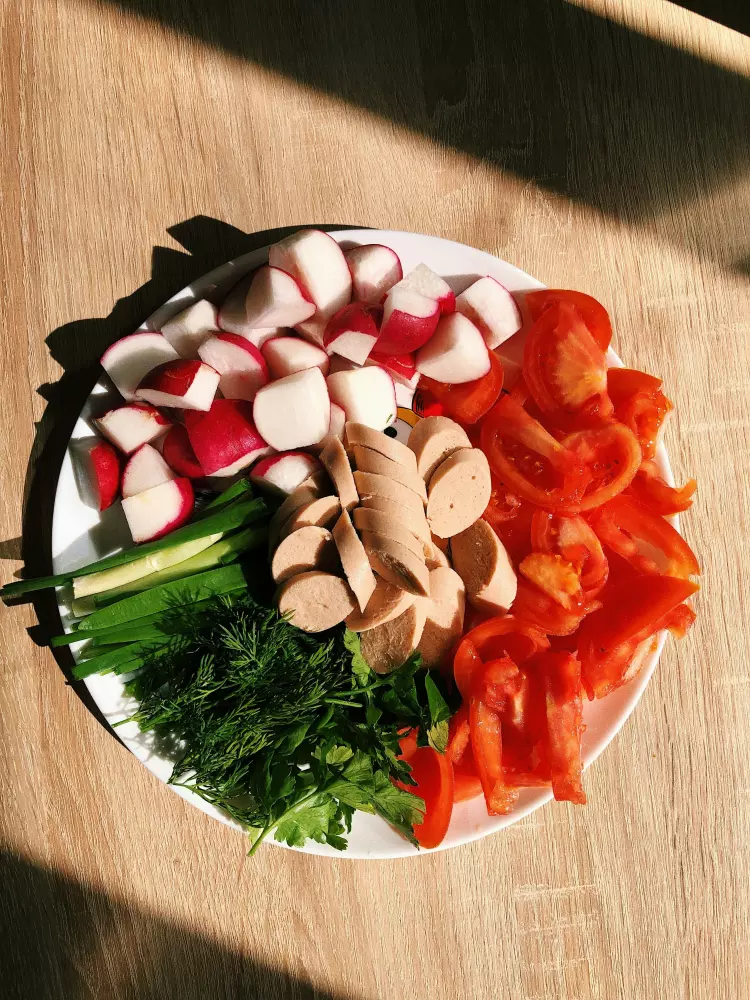 Ein weißer Teller, der mit vielen Gemüsesorten bedeckt ist, auf einem Holztisch.