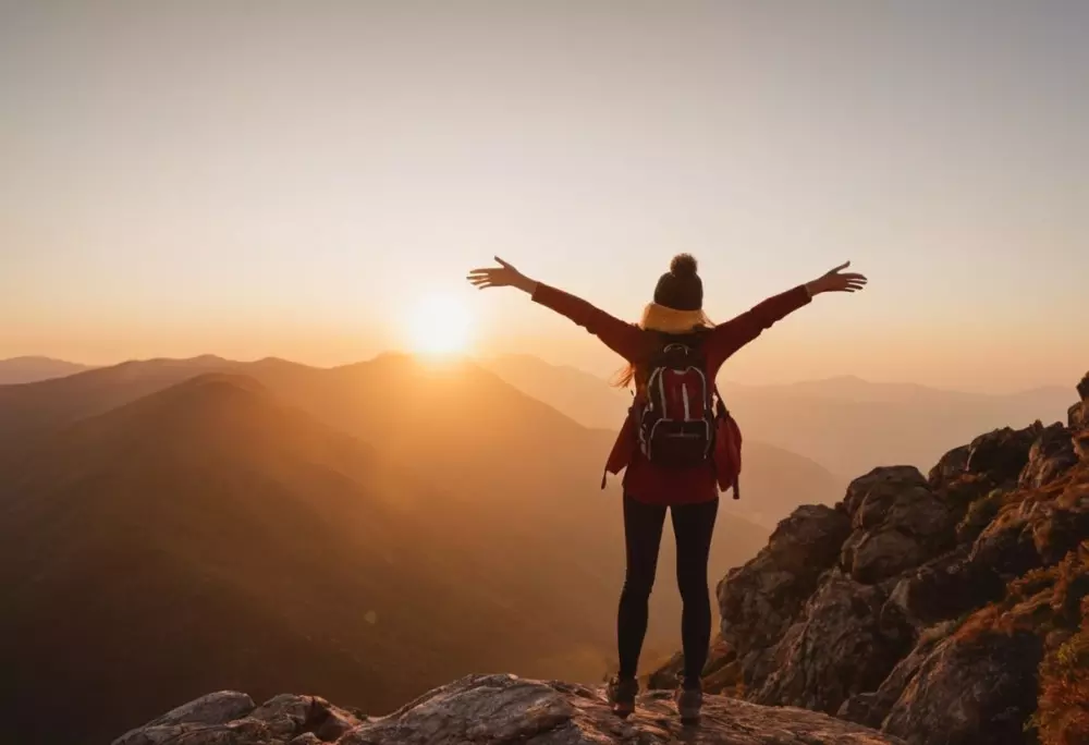 Frau genießt den Sonnenaufgang auf einem Berg, Arme weit ausgebreitet, umarmt neue Anfänge, fotografischer Stil mit einer DSLR, der Freiheit und Freude einfängt.