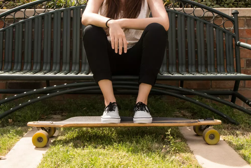 Eine Frau sitzt auf einer Bank mit ihren Füßen auf einem Skateboard.