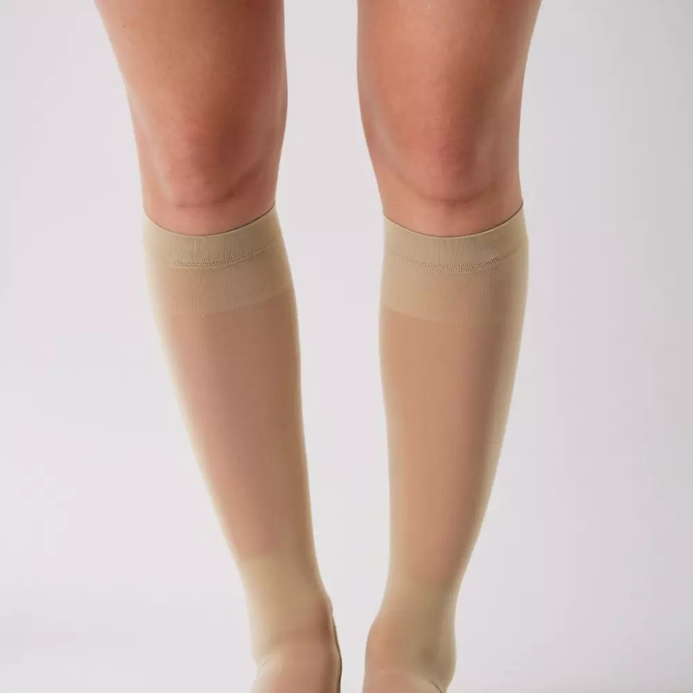 Eine Nahaufnahme von Beinen, die medizinische Kompressionsstrümpfe tragen, vor einem einfachen, neutralen Hintergrund mit weichem Studio-Licht, fotografiert mit hoher Detailgenauigkeit unter Verwendung eines Makroobjektivs für Klarheit und Präzision.