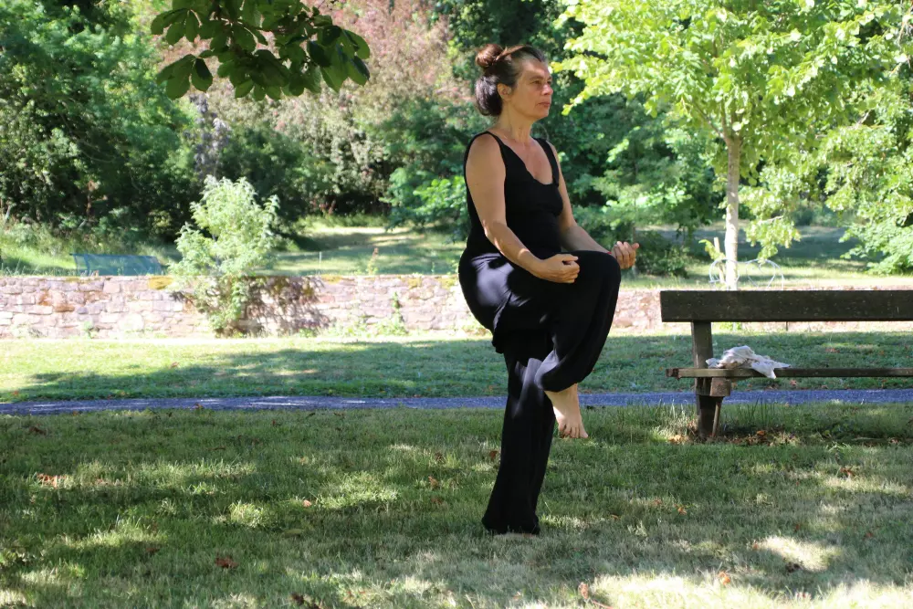 Eine Frau macht Yoga in einem Park in der Nähe einer Bank.