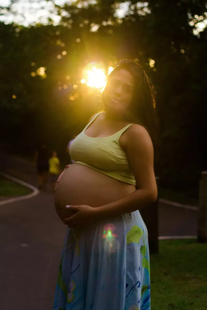 Eine schwangere Frau steht auf einem Weg bei Sonnenuntergang.